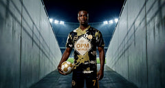 Man wearing a black and gold opium world football top in front of a football stadium with the Lights shining bright.