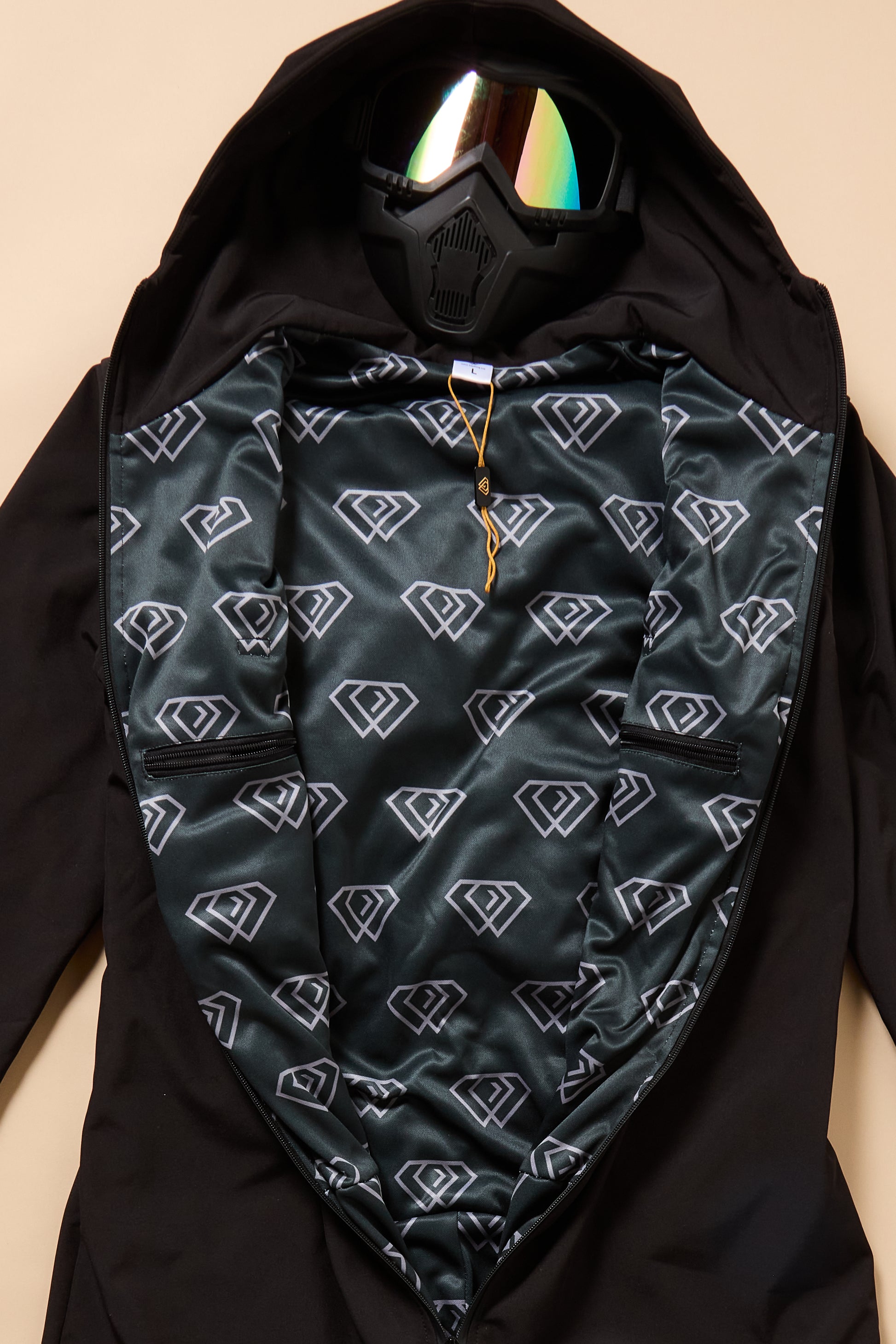 Black jacket with patterned inner lining and reflective goggles on a beige background