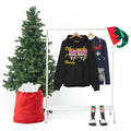 Black hooded sweatshirt with colorful graphic and text on hanger, Christmas decor nearby