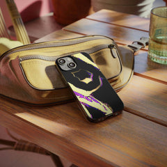 Abstract OPM design phone case with yellow, black, and purple on a table beside a beige bag