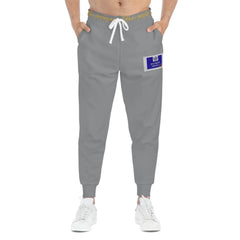 Grey joggers with drawstring waist, gold waistband text, and blue patch detail on left leg