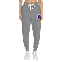 Grey joggers with yellow waistband text, drawstring, blue patch on thigh, modeled front view