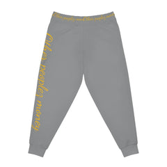 Gray joggers with yellow 'Other peoples money' script on leg and waistband, streetwear style.