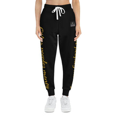 Black joggers with gold script lettering, drawstring waist, and white sneakers, urban streetwear style