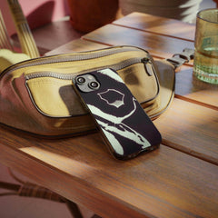 Abstract black and white phone case on tan bag, wooden table, lifestyle setting
