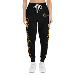 Black joggers with yellow script text, drawstring waist, worn by model standing