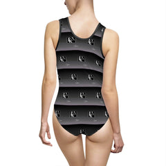 Woman wearing a black and grey one-piece swimsuit with abstract logo pattern, back view