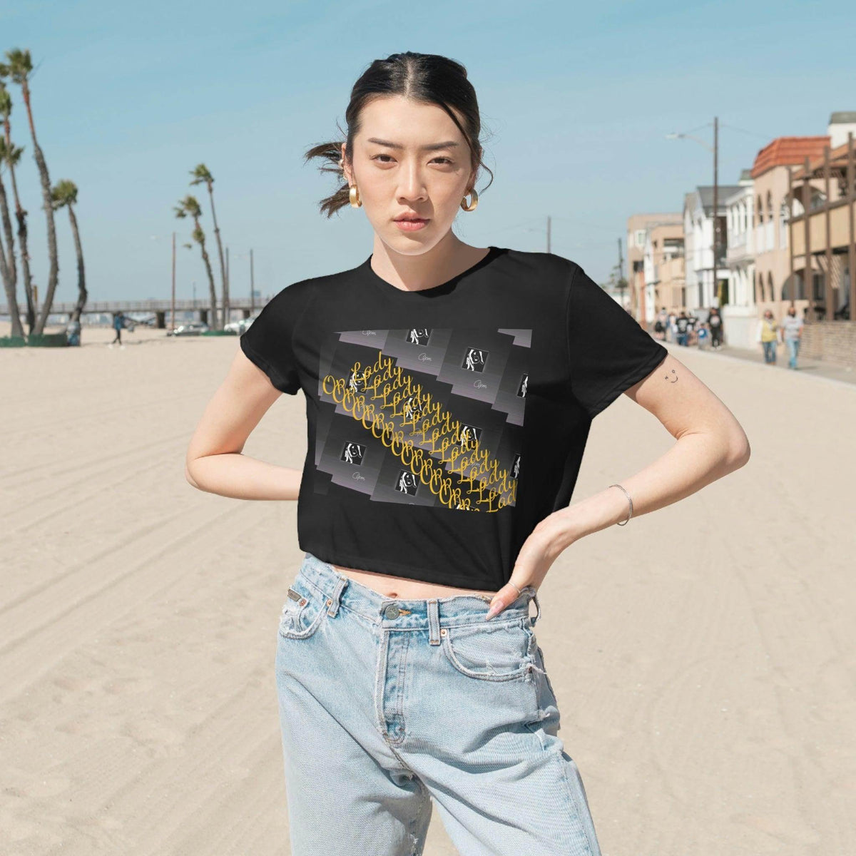 Woman wearing a black graphic cropped tee and jeans on a sunny beach street, urban streetwear style